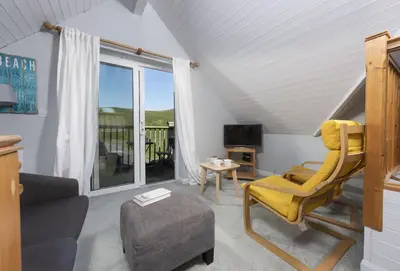 a living room with a yellow chair and a television at Rockside Studio in Polzeath
