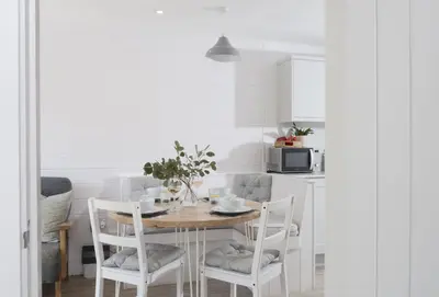 a dining room table with white chairs and a kitchen at Robin in Polzeath