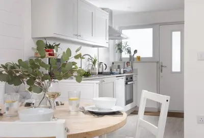 a kitchen with white cabinets and a wooden table at Robin in Polzeath
