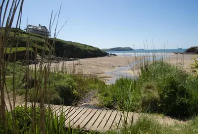 a wooden path to the beach with a house in the background at The Perch Studio in Polzeath