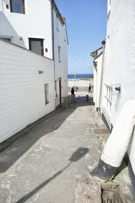 an empty street next to a white building and the beach at Silver Seahorse a classic fishermans cottage in St Ives