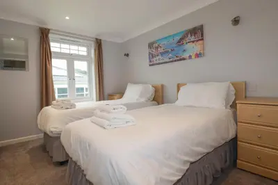 two beds in a bedroom with white sheets and towels at Satinwood in Newquay
