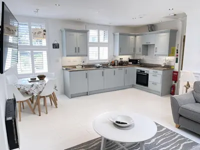 a kitchen and living room with white cabinets and a table at 4 Hazelbury House - a tranquil hidden gem in St Ives