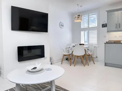 a white living room with a table and a tv at 4 Hazelbury House - a tranquil hidden gem in St Ives