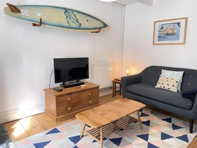 a living room with a couch and a surfboard hanging on the wall at 2 Upper Meadow - near to Porthmeor Beach in St Ives