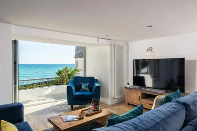 a living room with a blue couch and a tv and the ocean at Blue Mist House in St Ives