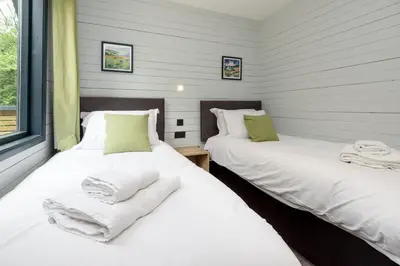 two beds in a room with white sheets and towels at Cardinham Lodge, The Vale, Cornwall in Looe
