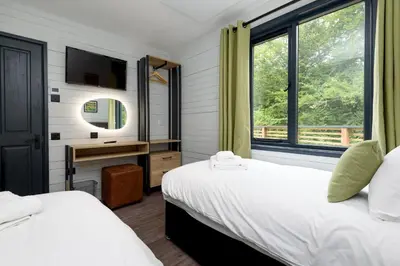a bedroom with two beds and a desk with a mirror at Cardinham Lodge, The Vale, Cornwall in Looe