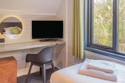 a room with a bed and a television and a chair at Cardinham Lodge, The Vale, Cornwall in Looe