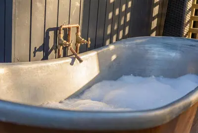a bath tub filled with water next to a faucet at Cardinham Lodge, The Vale, Cornwall in Looe