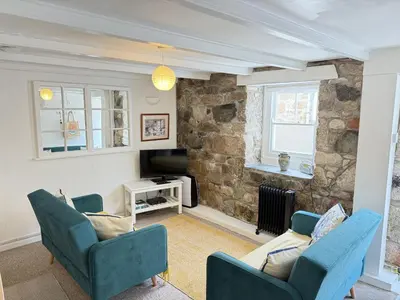 a living room with two blue chairs and a stone wall at Lower Deck in St Ives