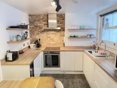 a kitchen with white cabinets and a brick wall at The Bolthole, a cosy, contemporary cottage! in St Ives