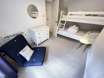 a small room with two bunk beds and a chair at The Bolthole, a cosy, contemporary cottage! in St Ives