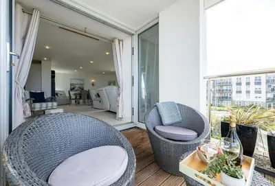 a balcony with a wicker chair and a living room at Number 2 in Lusty Glaze, Newquay in Newquay