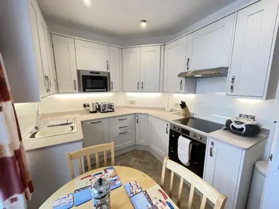 a kitchen with white cabinets and a table and chairs at Upper Seaview in St Ives