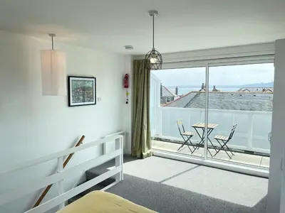 a bedroom with a bed and a balcony with a table and chairs at 26 Piazza - stunning seaviews of Porthmeor beach in St Ives