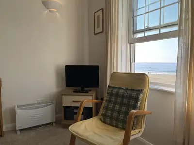 a room with a chair and a television and a window at 4 Crusoes - beachside apartment in St Ives