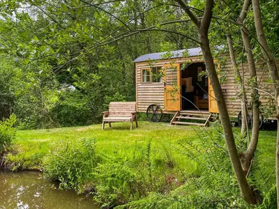 a wooden cabin with a bench next to a river at The Goose Nest in Cardinham