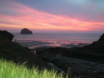 a sunset over a beach with a rock in the ocean at Cottage On The Square in Camelford