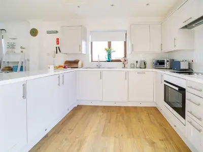a white kitchen with white cabinets and a wooden floor at Wenlock in Polzeath