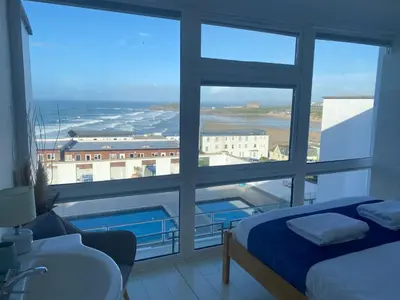 a room with a large window with a bed and a sink at Stunning Sea View Apartment in Newquay with 2 Heated Pools in Crantock
