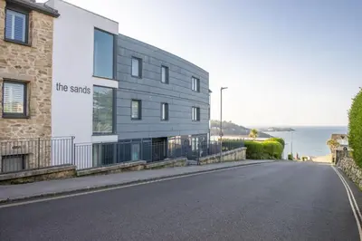 a building on the side of a road next to the ocean at Spectacular Sea Views, Wi-Fi, Parking in Carbis Bay
