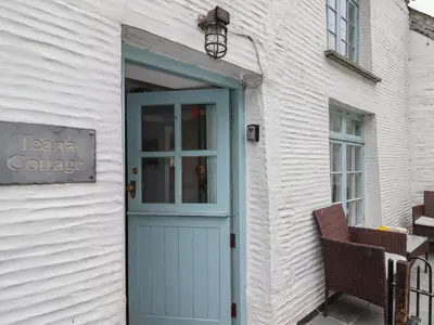 a white building with a blue door and a chair at Teana Cottage in Looe
