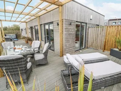 a patio with tables and chairs on a wooden deck at Petroc in Redruth