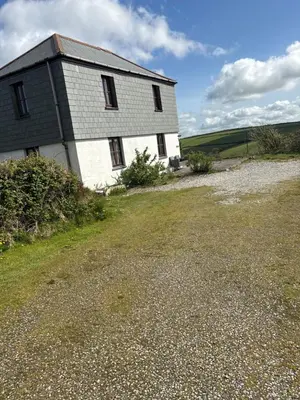 a white building with a roof on a field at Tregatherall Barn in Boscastle