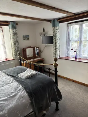 a bedroom with a bed and a television and windows at Tregatherall Barn in Boscastle