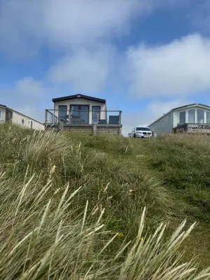 a house on top of a grassy hill with a car at Seaview Caravan, Perran Sands in Perranporth