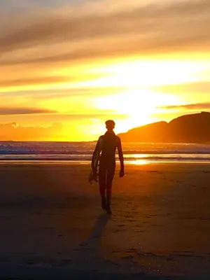 a person walking on the beach with a surfboard at Little Nampara Cottage in Portreath