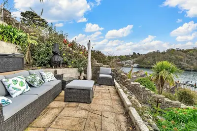 a patio with a couch and chairs next to a river at Finest Retreats - Garden Cottage in Fowey in Fowey
