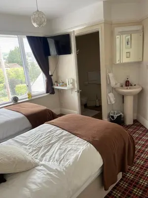 a bedroom with a bed and a bathroom with a sink at Cornerways Guest House St Austell Cornwall in St Austell