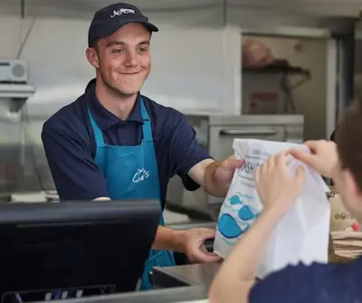 a man in a kitchen handing a woman a piece of paper at Dune Breeze-Haven Perran Sands Holiday Park in Perranporth