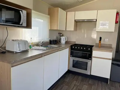 a kitchen with white cabinets and a sink and a microwave at Newquay - Pet Friendly 6 Berth Caravan in Newquay