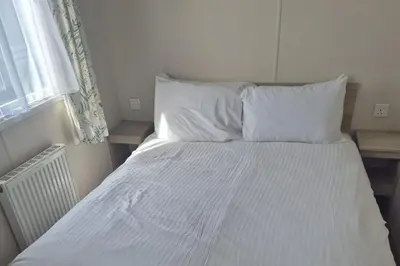 a bed with white sheets and pillows next to a window at Newquay - Pet Friendly 6 Berth Caravan in Newquay