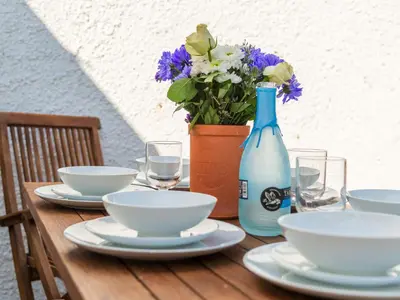 a wooden table with plates and a vase with flowers at Holiday Home Seaforth by Interhome in Gorran Haven