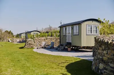 a tiny house in a yard next to a stone wall at Shepherds Huts at The Cornish Arms in St Merryn