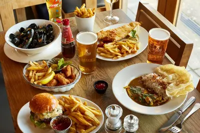 a wooden table topped with plates of food and drinks at Shepherds Huts at The Cornish Arms in St Merryn