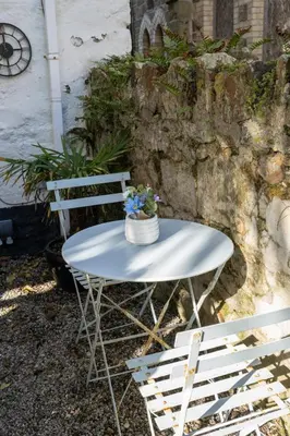 a white table and two chairs in front of a stone wall at Palm Haven House - Luxury family-friendly Newquay surf house near Porth Beach perfect for walking, pets, exploring in Newquay