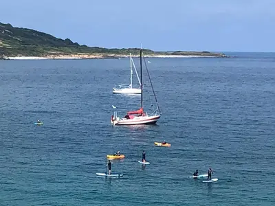 a group of people on surfboards in the water with a sail boat at Celtic Longhouse Tent at Coverack Camping in Coverack