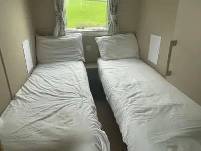 two beds in a small room with a window at Caravan 163 sleeps up to 8 guests in Newquay