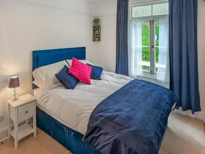 a bedroom with a blue and white bed and a window at Denzell in Looe