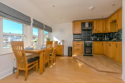 a kitchen with wooden cabinets and a table with chairs at Harts Loft - On Beach - Panoramic Sea Views - By Harbour in St Ives