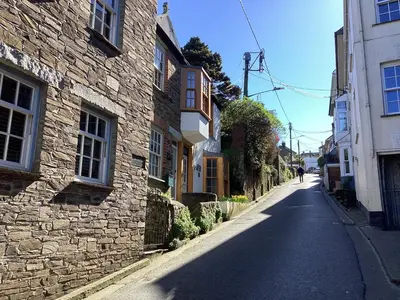 a person walking down a street next to a stone building at Charming Fishing Cottage in Polruan