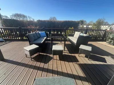 a deck with two couches and a table and chairs at Sunset family lodge private garden private parking in Saint Columb Minor