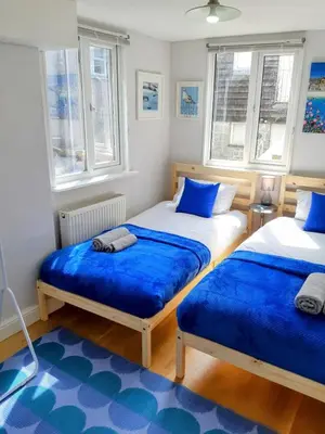 two beds in a bedroom with blue sheets and windows at Chapel Street Retreat in St Ives