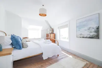a white bedroom with a bed and a painting on the wall at Hilldene in Tintagel