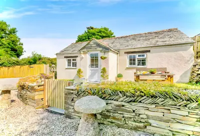 a cottage with a stone fence and a bench at Hawthorn in Bude